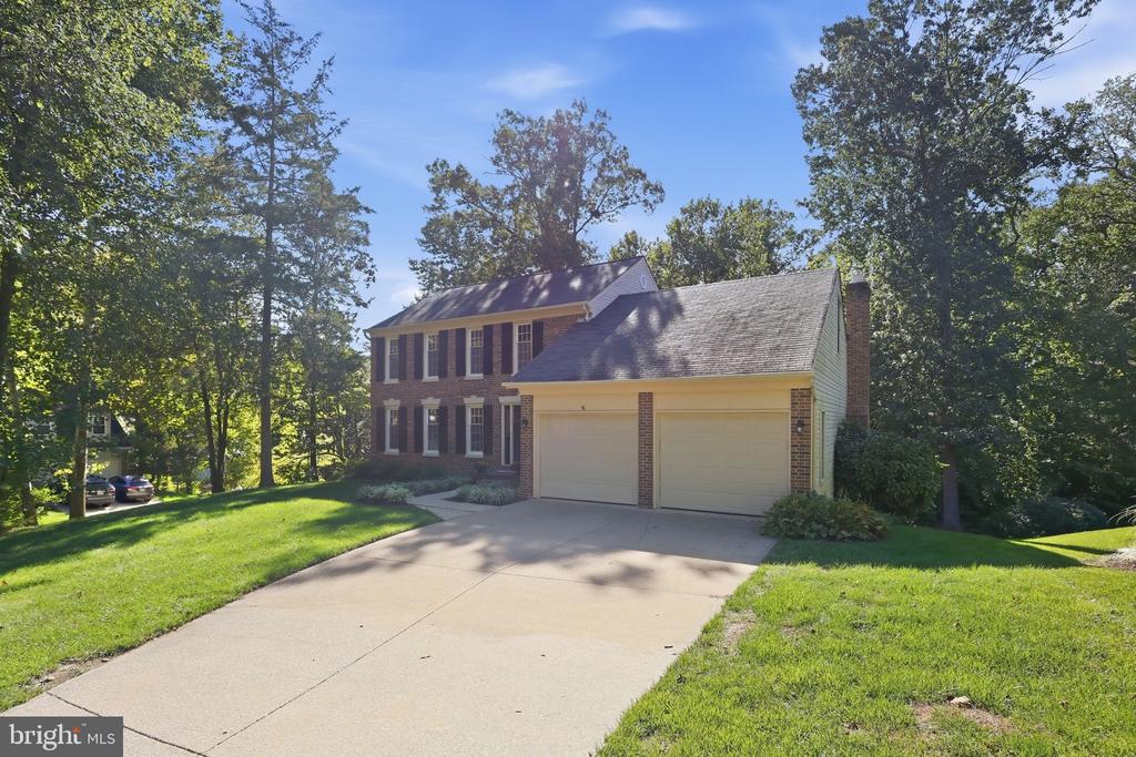 Two-story brick home with a two-car garage, broad driveway, and mature trees.