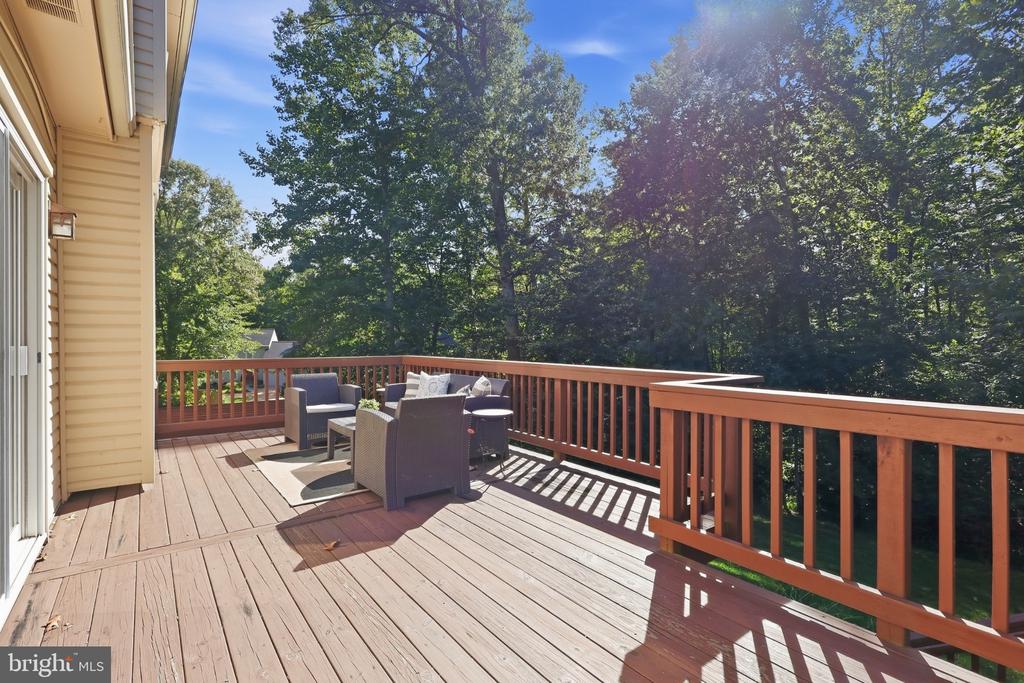 Wooden deck with outdoor seating overlooking dense leafy trees.