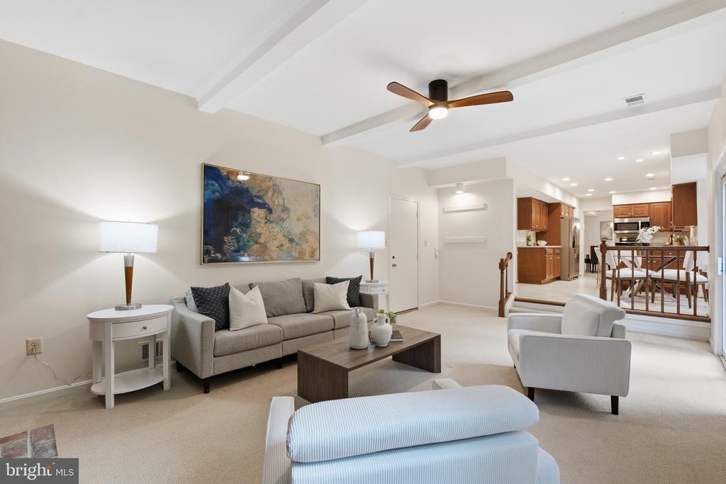 Living room with gray sofa and white armchairs, opening onto a dining area and kitchen.