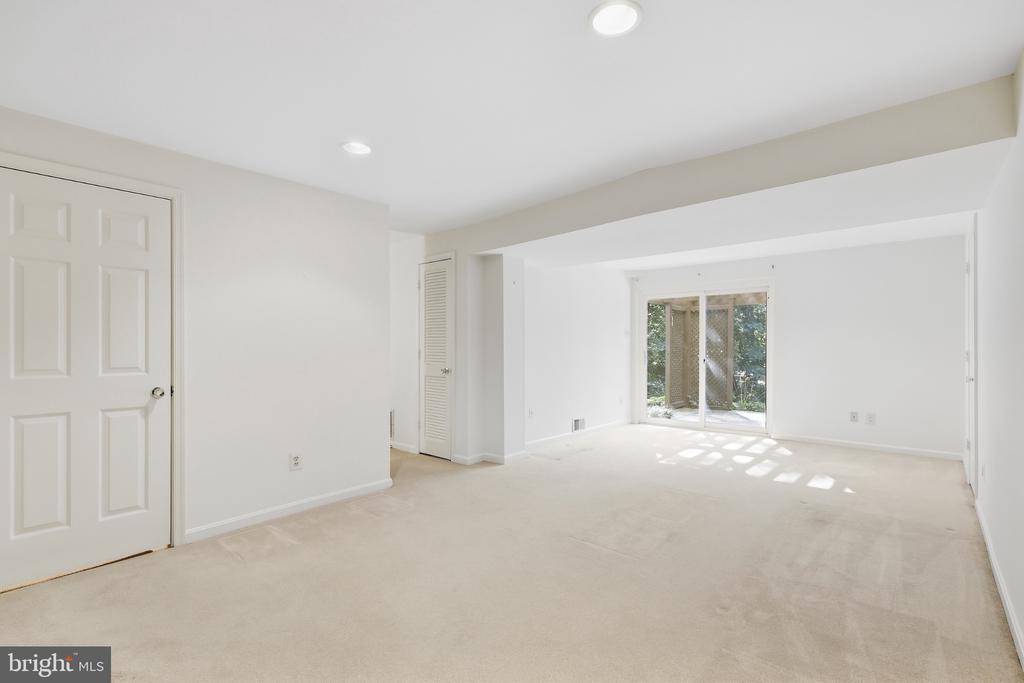 Vacant carpeted living room with recessed lights and sliding glass doors overlooking greenery.