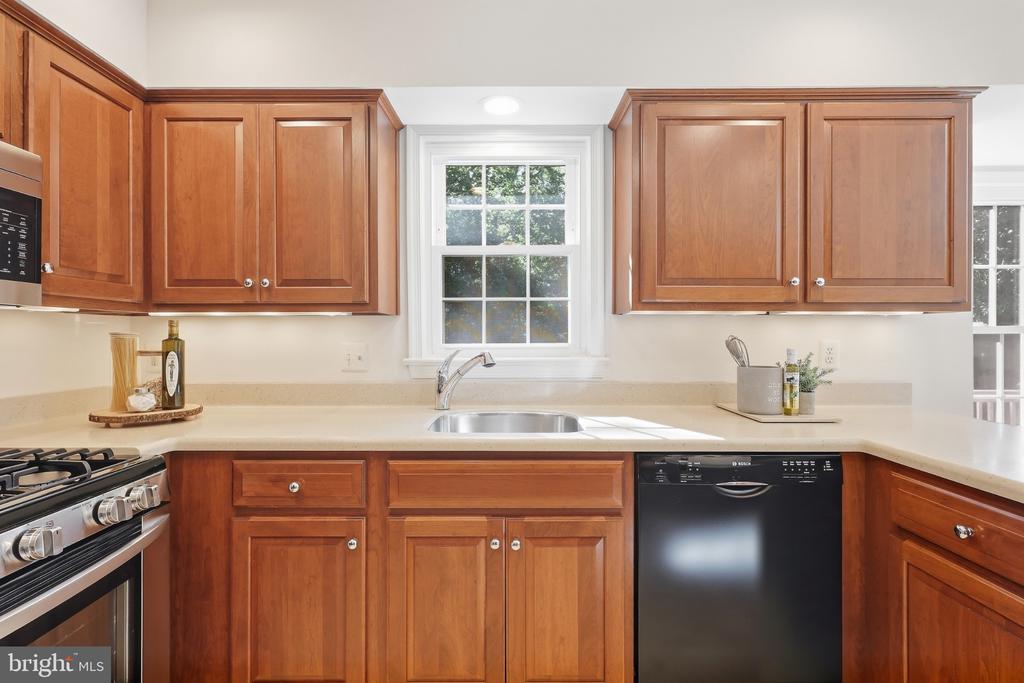 Kitchen with warm wood cabinets, a window above the sink, a gas range, and a black dishwasher.