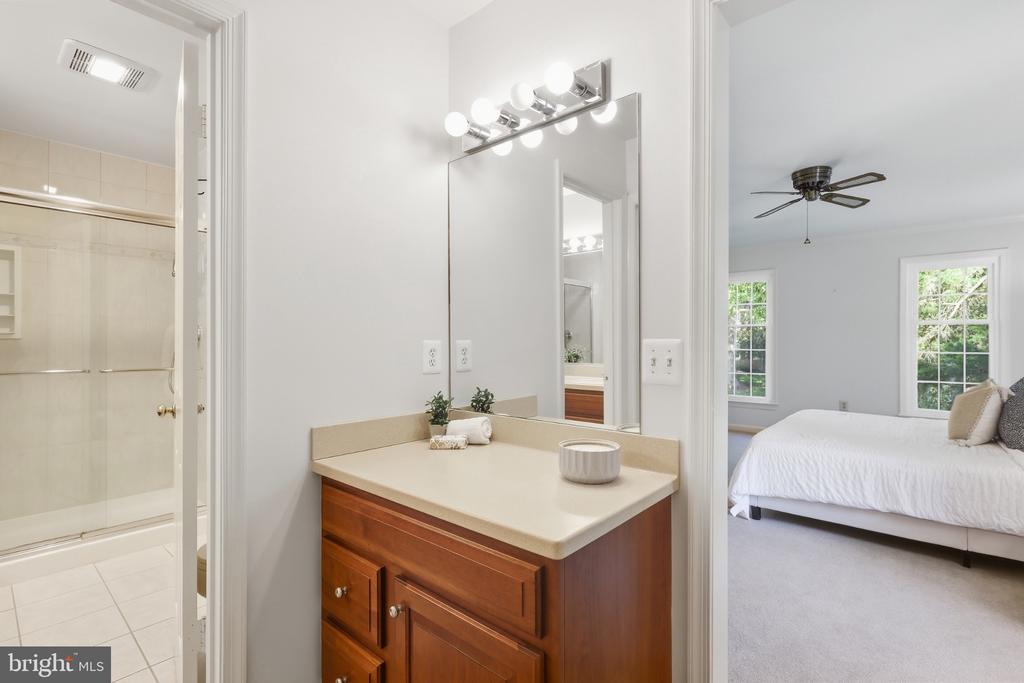 Bathroom vanity with a beige countertop, tiled shower, and adjoining bedroom.