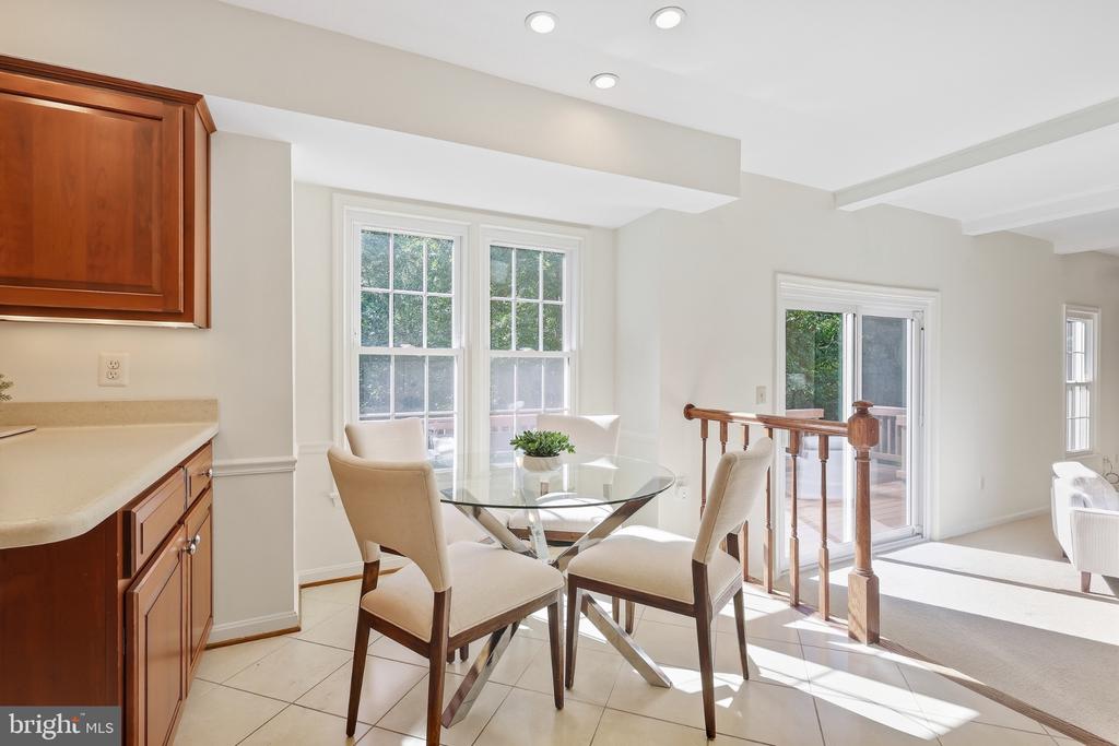 Dining area with a round glass table, upholstered chairs, and large windows beside sliding doors to a deck.