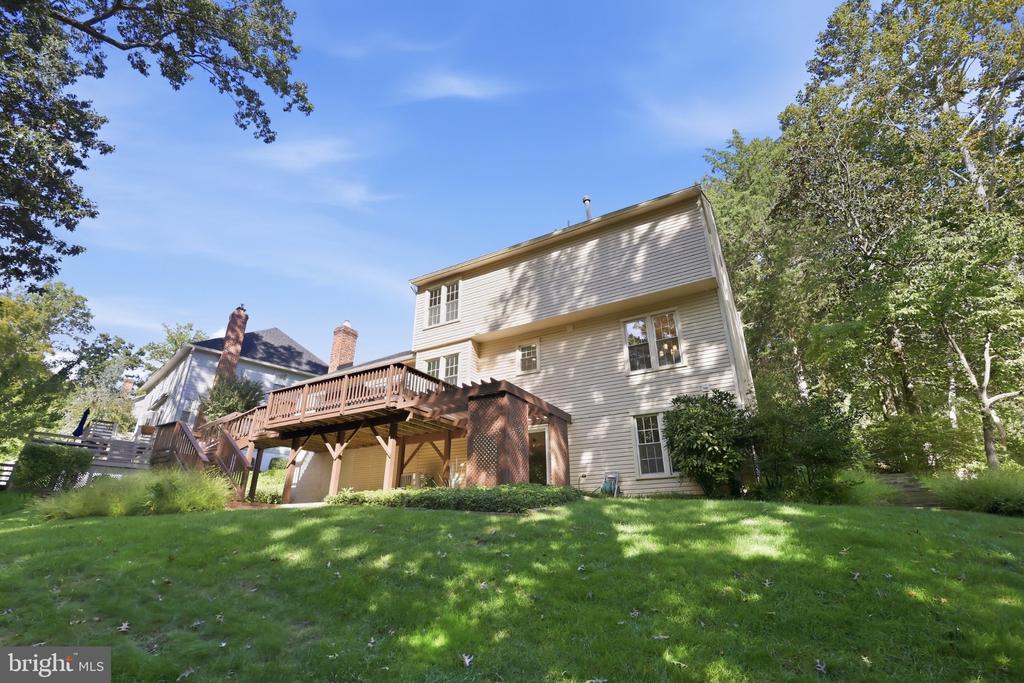 Rear of a two-story house with a raised wooden deck and a shaded lawn.