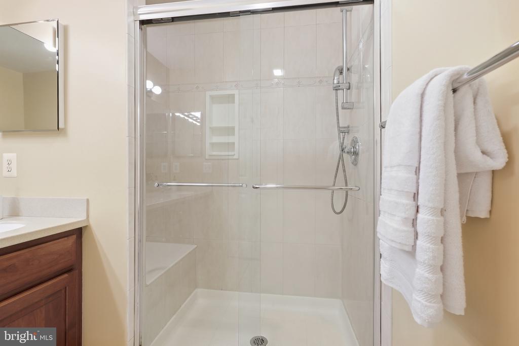 Walk-in shower with light tile walls, a built-in bench, chrome fixtures, and white towels.