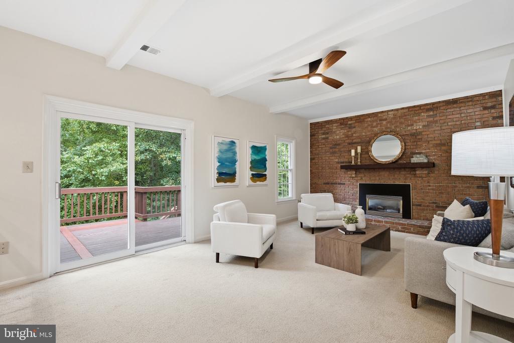 Living room with exposed brick fireplace, white seating, and sliding doors to a wooded deck.
