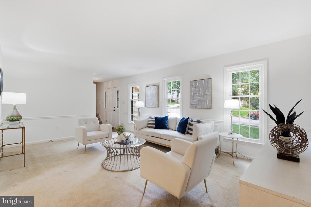 Staged living room with cream seating, a round glass coffee table, and large windows overlooking greenery.