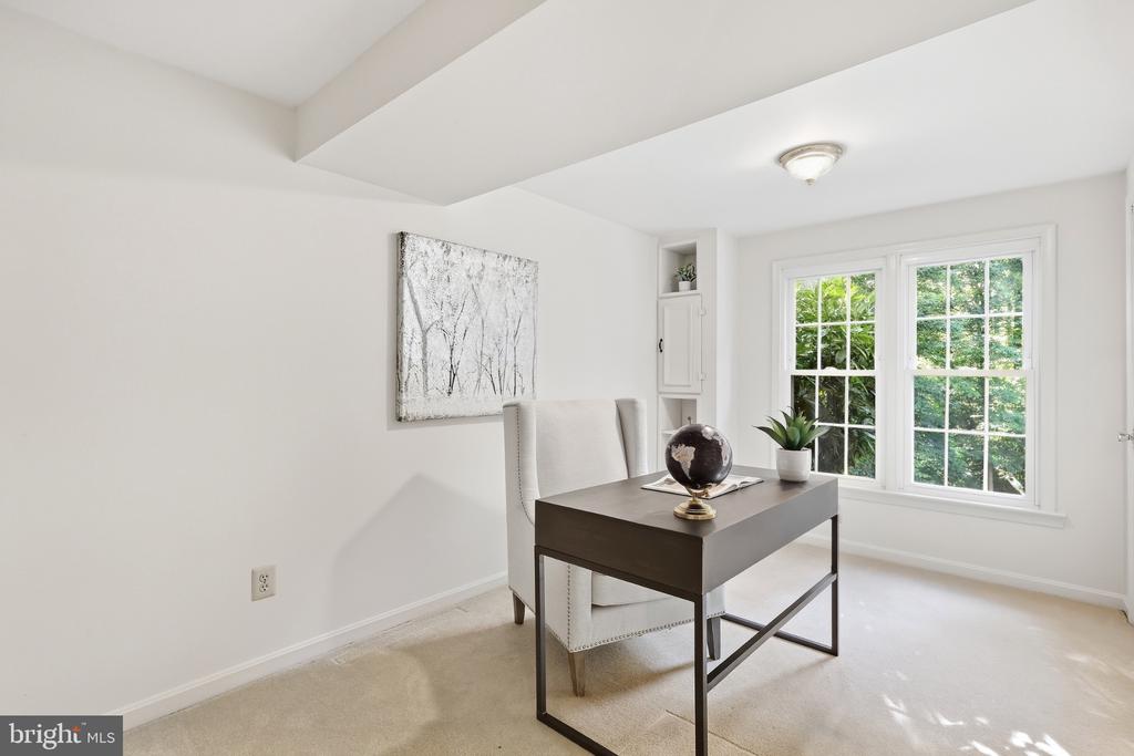 Staged home office with a dark desk and large windows overlooking greenery.