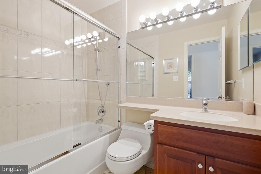 Bathroom with a glass-enclosed tub, large mirror, and wood vanity.