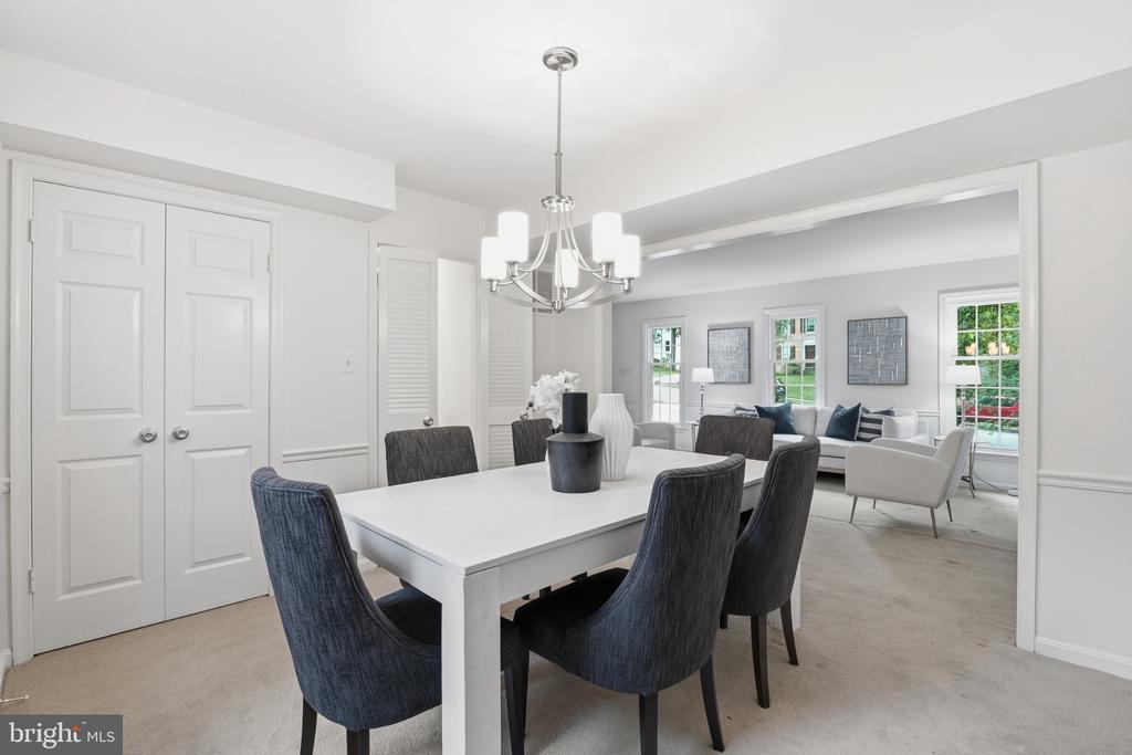 Dining room with a white table, dark upholstered chairs, chandelier, and adjoining sitting area.