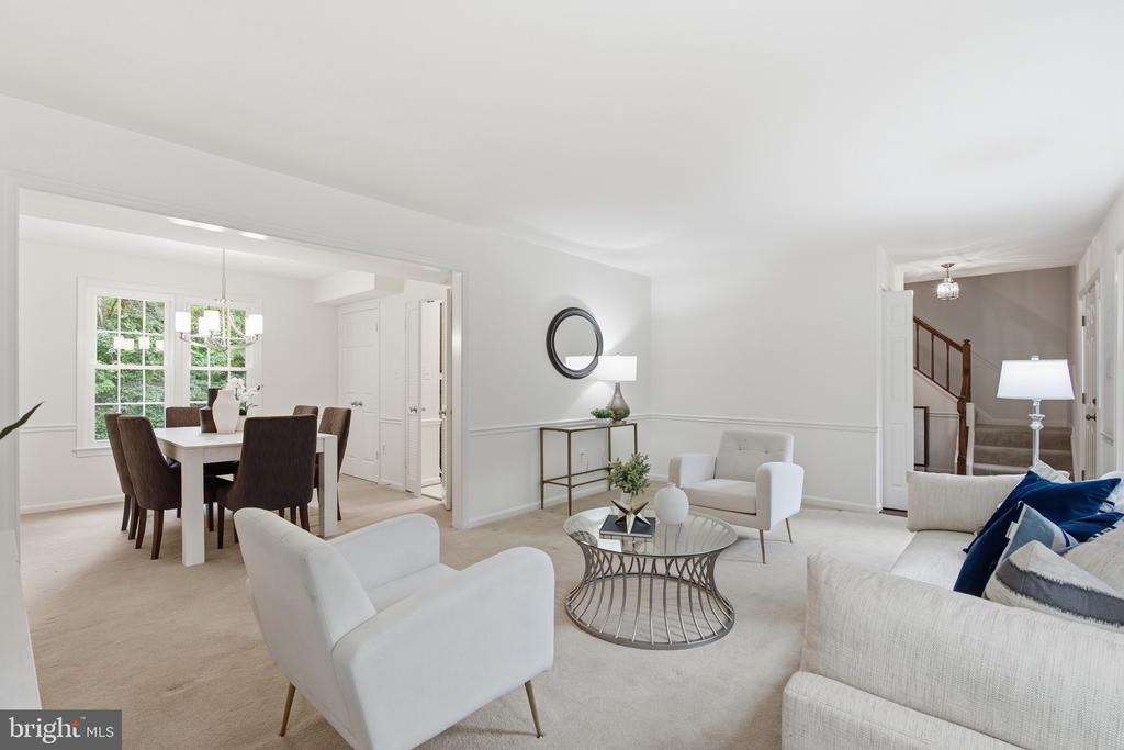 Staged living room with a glass coffee table, opening to a dining area with large windows.