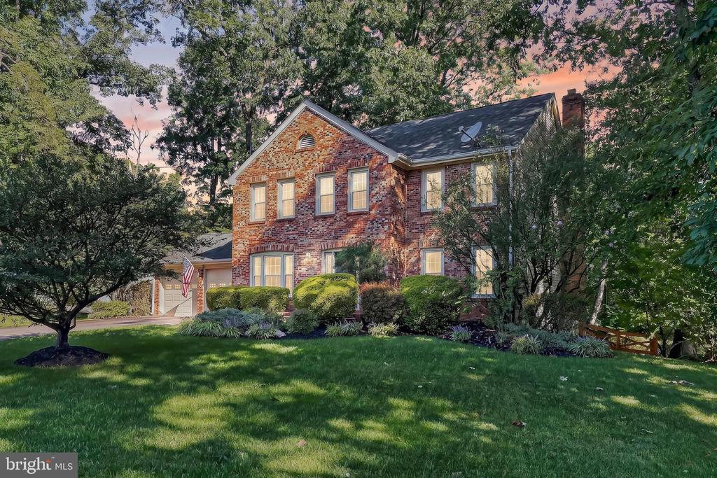 Two-story brick house with an attached garage, landscaped garden, and mature trees.