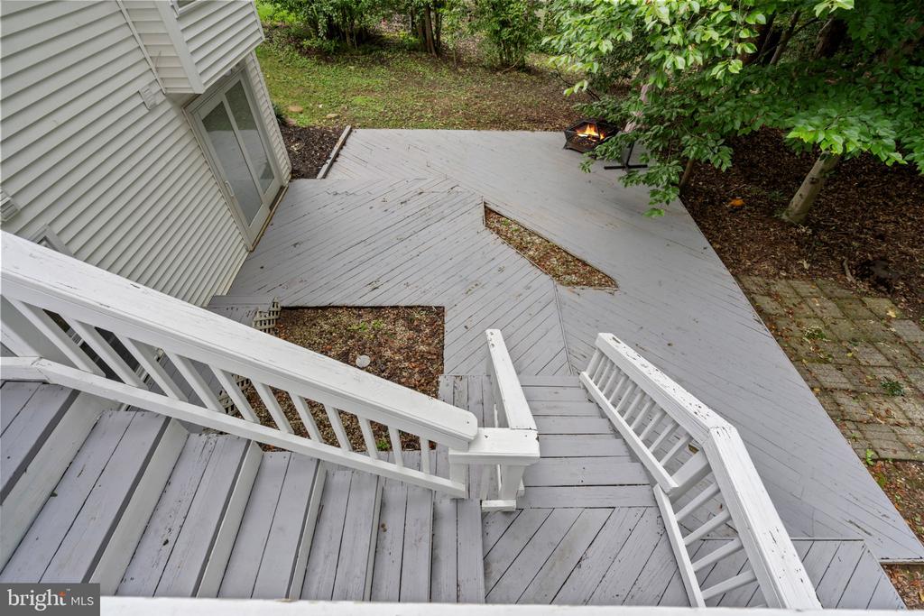 Backyard deck with broad gray boards, white railings, stairs, and a fire pit beside a leafy yard.