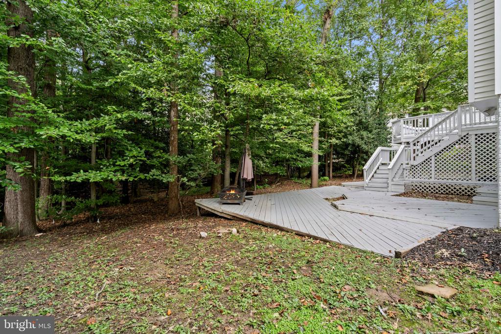 Backyard deck with a fire pit and closed umbrella, surrounded by mature trees.