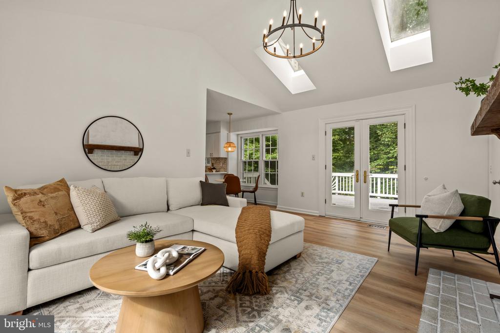 Living room with a white sectional, vaulted skylit ceiling, and French doors opening to a deck.
