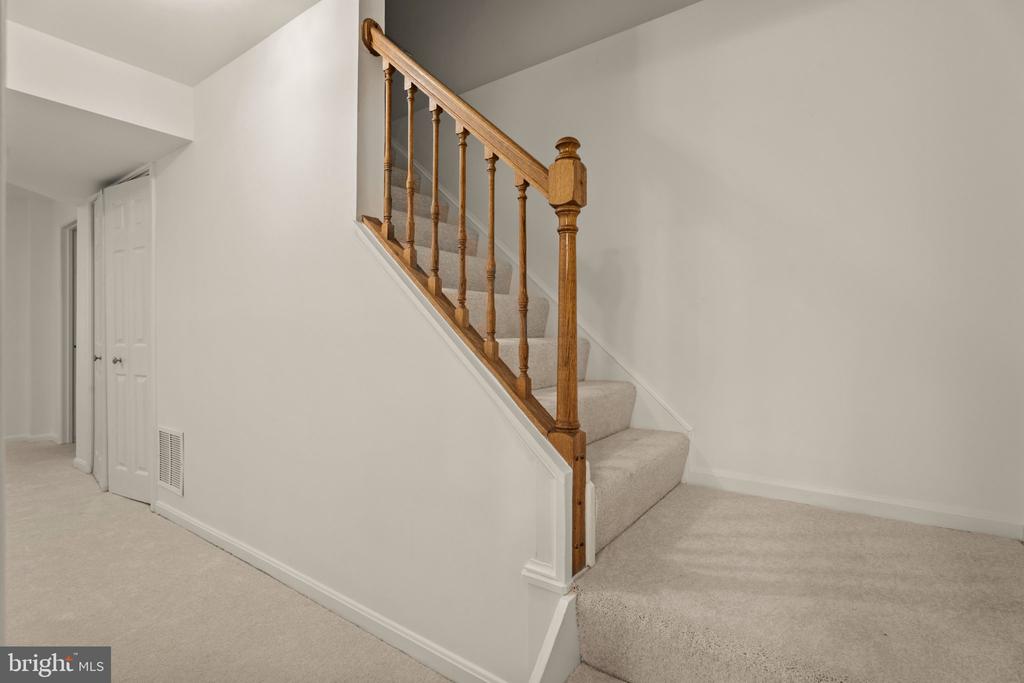 Carpeted staircase with a wooden railing beside a white-walled landing.