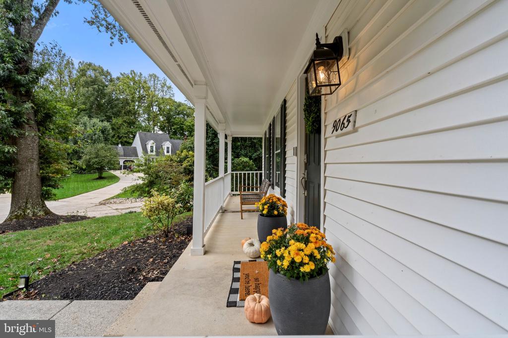 White house front porch with yellow chrysanthemums, pumpkins, and the number 9065 beside the door.