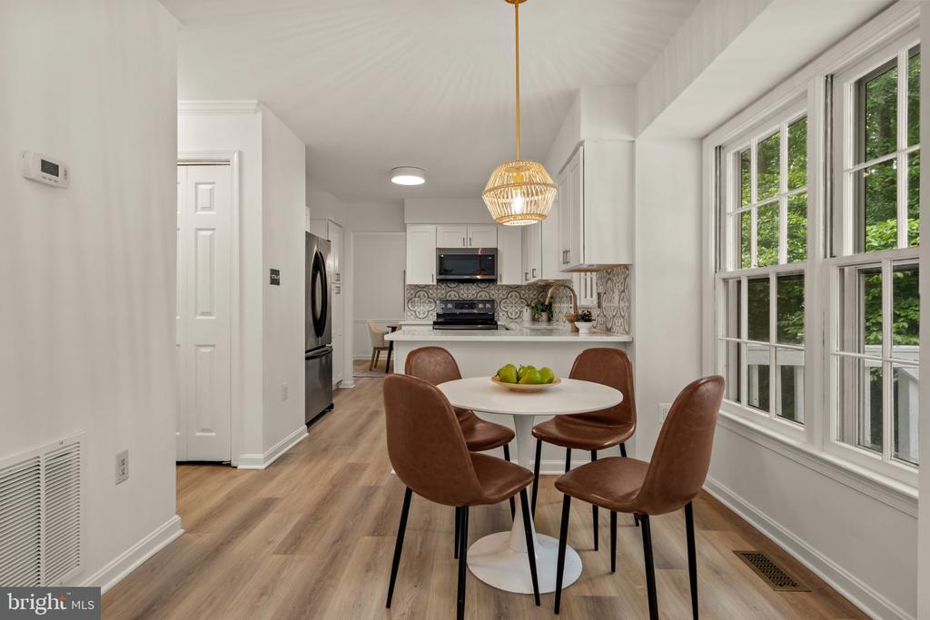Kitchen and dining area with white cabinetry, patterned backsplash, round table, and large windows.