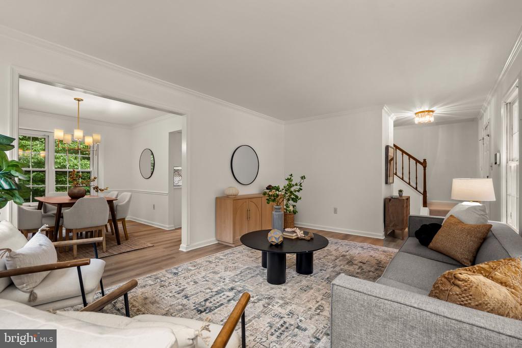 Staged living and dining room with a round black coffee table and staircase in the background.