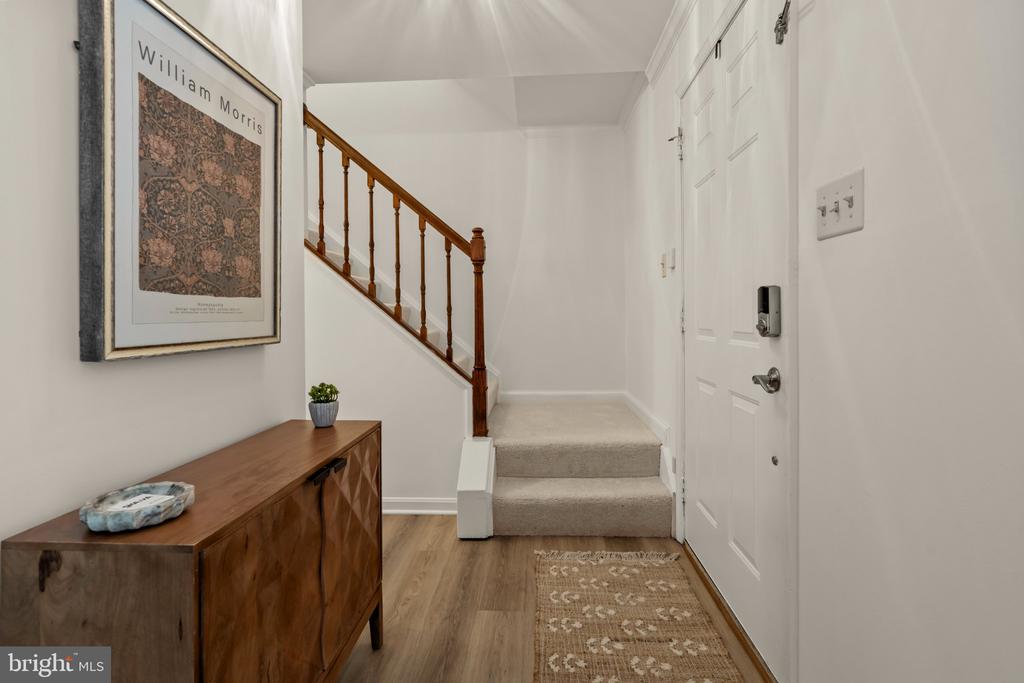 Entryway with a white front door, carpeted stairs, wood railing, and console table.