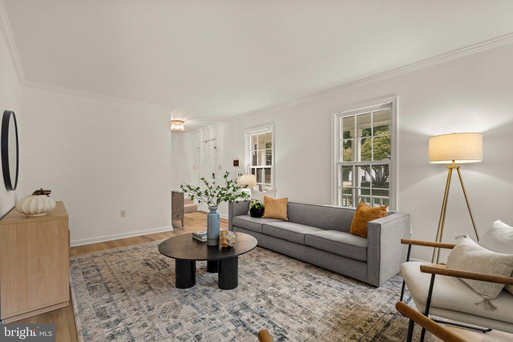 Staged living room with a gray sofa, patterned rug, and tall windows overlooking greenery.