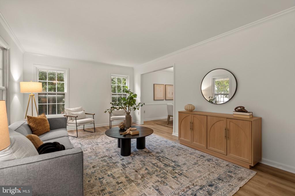 Staged living room with a gray sectional, patterned rug, and wood sideboard beneath a round mirror.