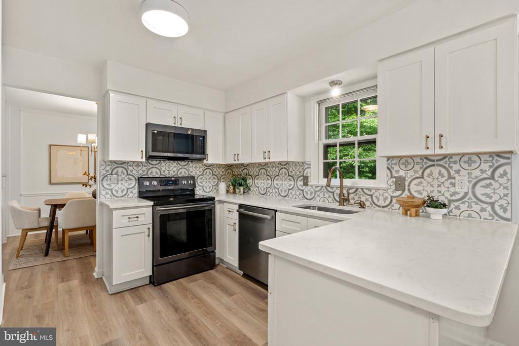 Kitchen with white cabinets, black appliances, patterned backsplash, and a large peninsula.