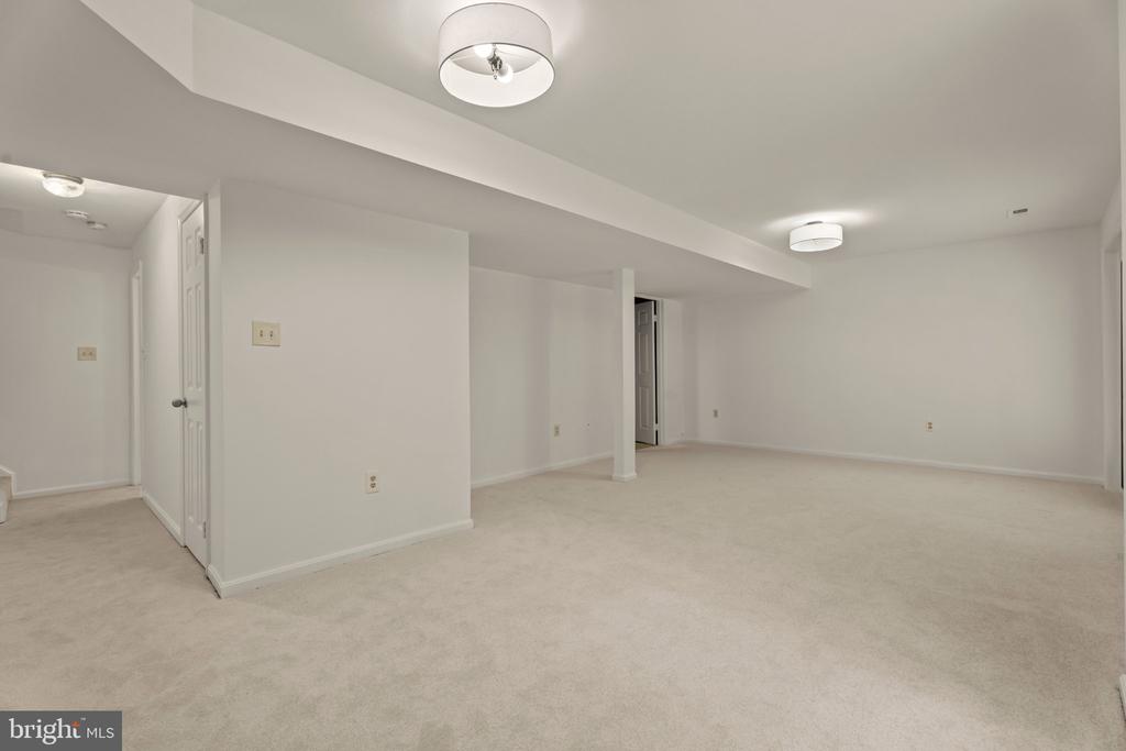 Empty carpeted room with white walls, ceiling lights, and open passageways.