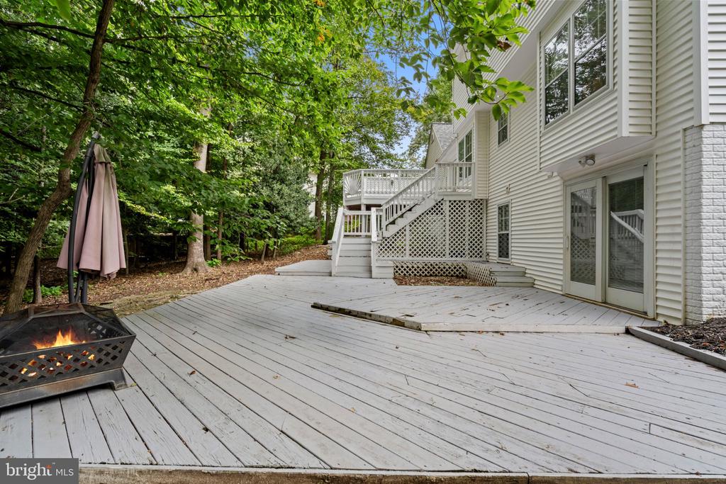 White backyard deck beside the house, with stairs, a fire pit, and mature trees.