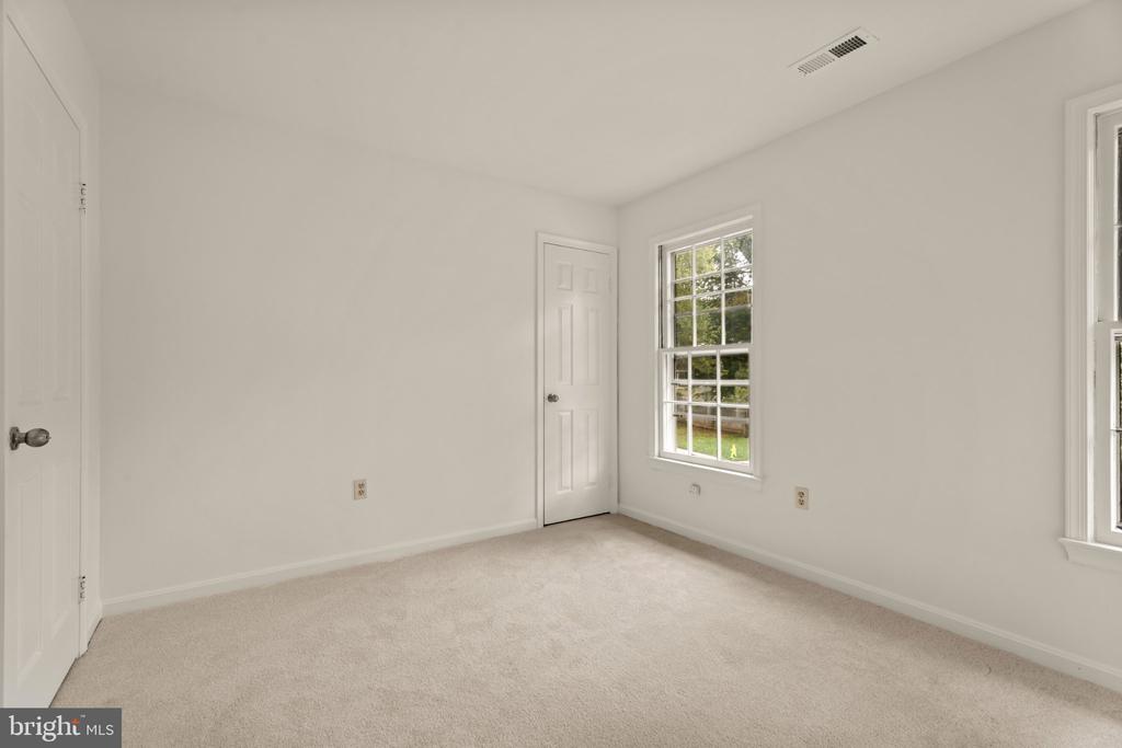 Empty carpeted bedroom with white walls, two windows, and two doors.