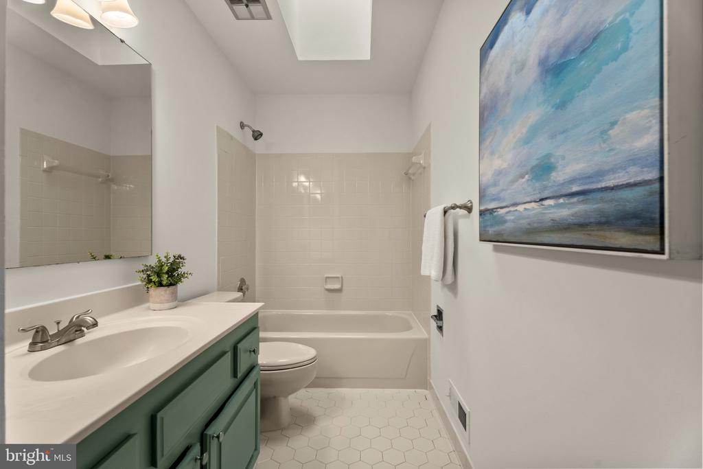 Bathroom with a green vanity, tiled bathtub surround, and blue seascape artwork.