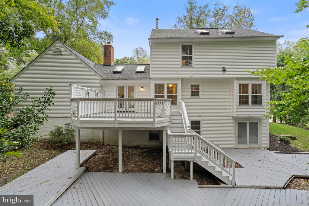 Rear of a two-story house with an elevated deck and broad ground-level deck.