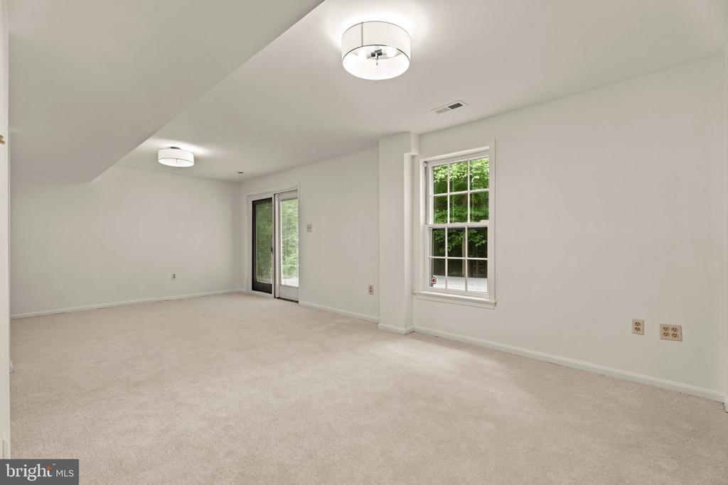 Empty carpeted room with a large window, sliding glass doors, and ceiling lights.