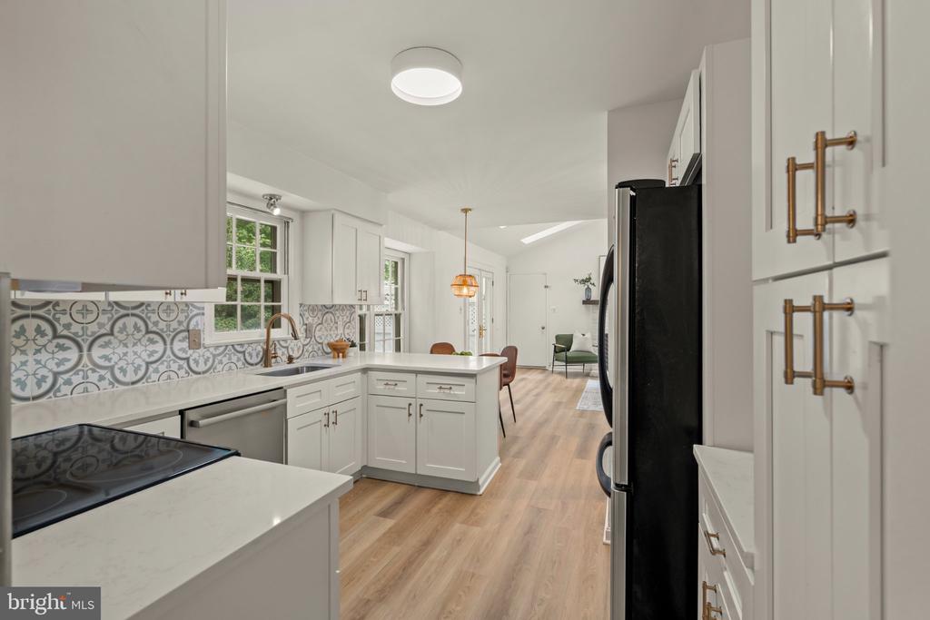 Bright white kitchen with patterned tile backsplash, brass hardware, and an island opening to a sitting area.