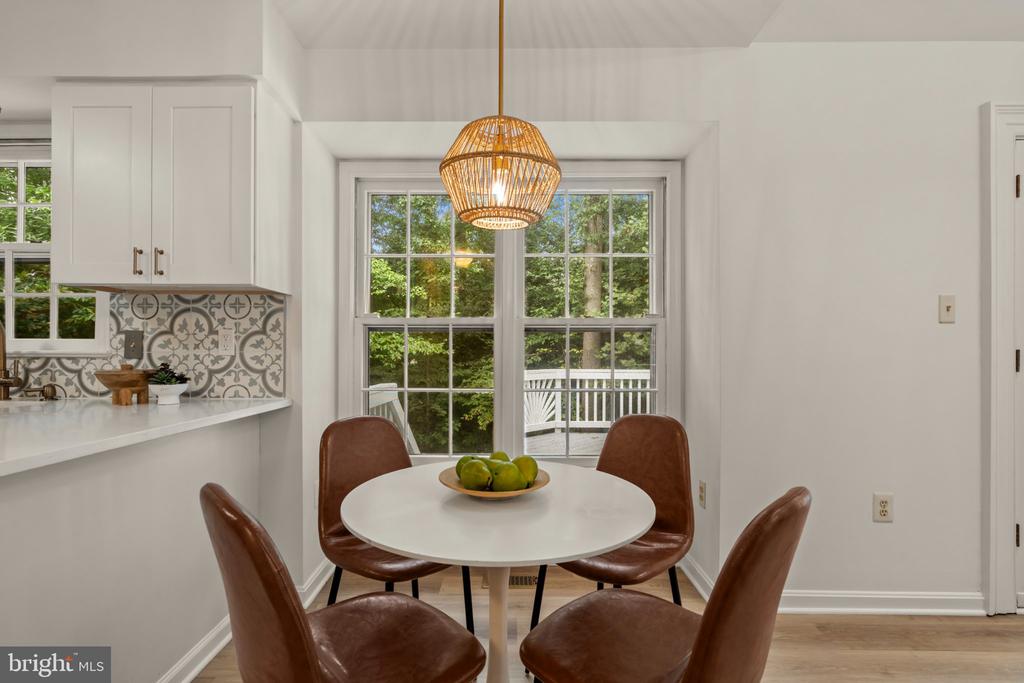 Dining nook with a round table, brown leather chairs, woven pendant light, and windows overlooking trees.