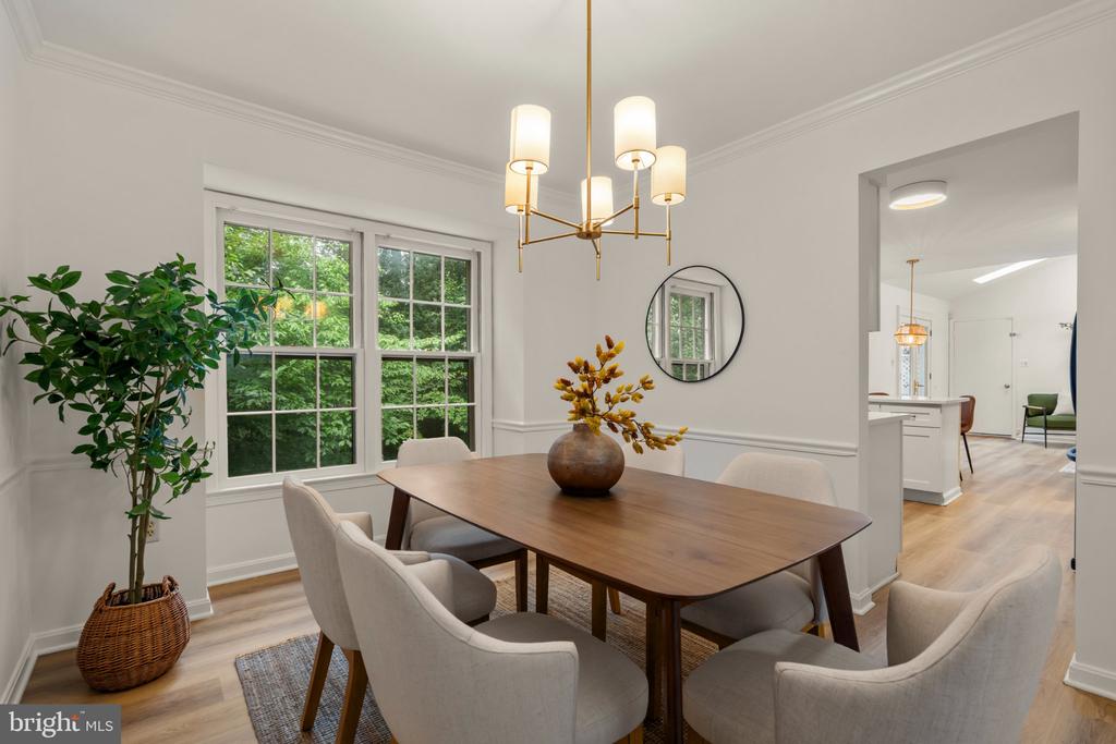 Dining room with a wood table and upholstered chairs beside large windows.