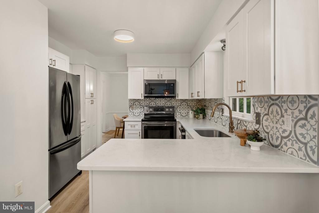 Kitchen with white cabinets, stainless appliances, a broad peninsula, and patterned tile backsplash.