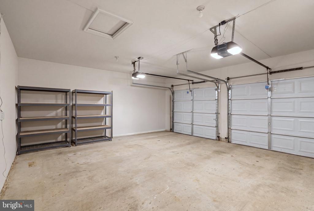 Two-car garage with white overhead doors, ceiling-mounted openers, and metal storage shelves.