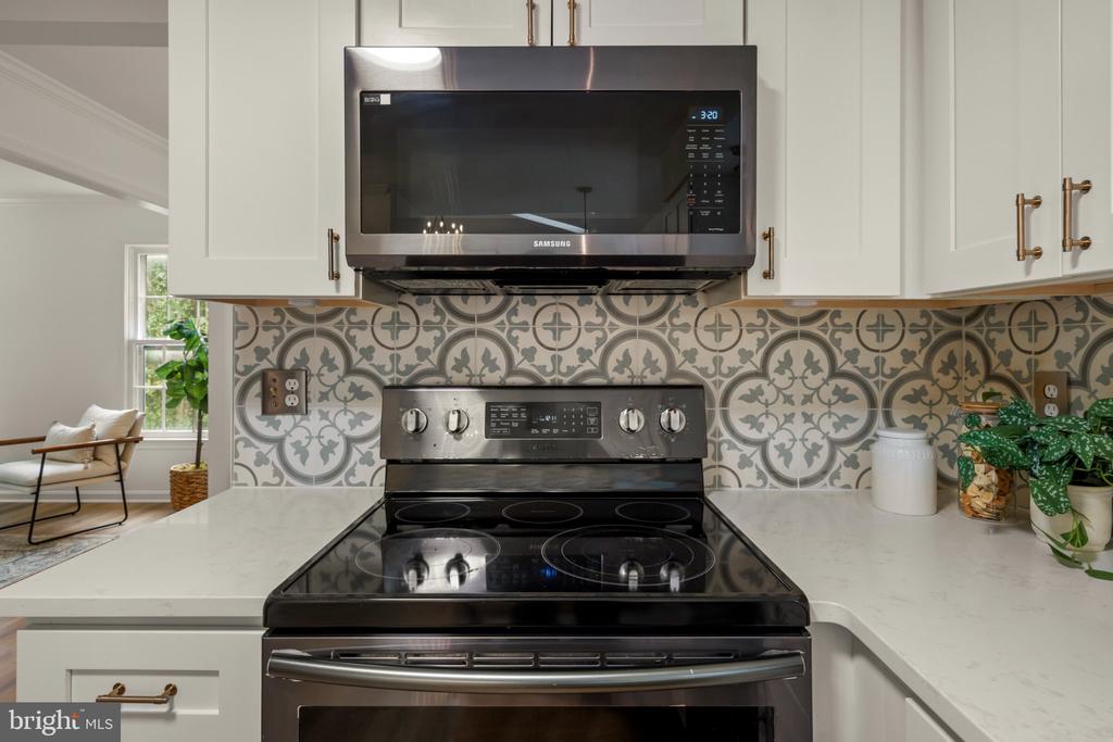 Kitchen with a black range, white cabinetry, and patterned gray tile backsplash.
