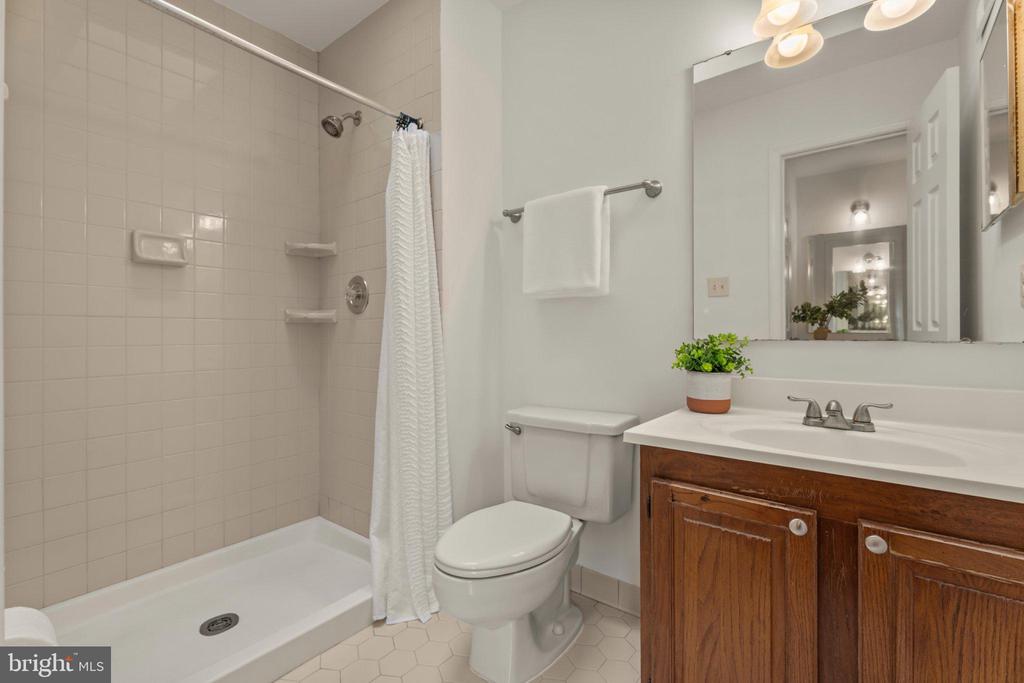 Bathroom with tiled tub and shower, toilet, and dark wood vanity topped with a white counter.