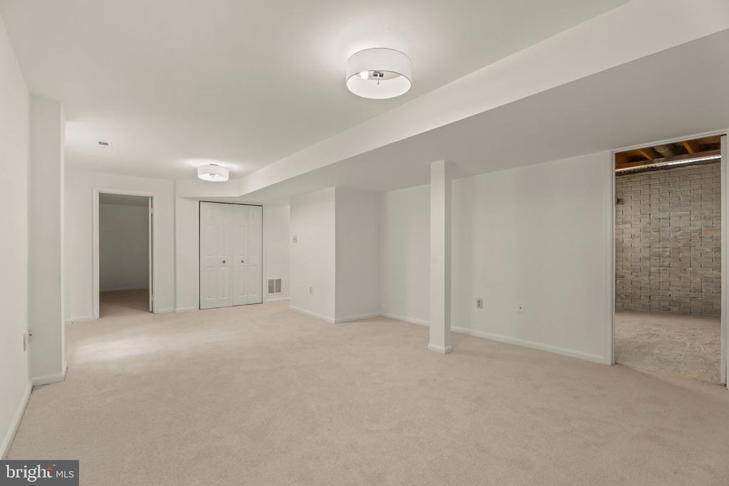 Empty carpeted basement with a white closet and an adjoining storage area with exposed brick.