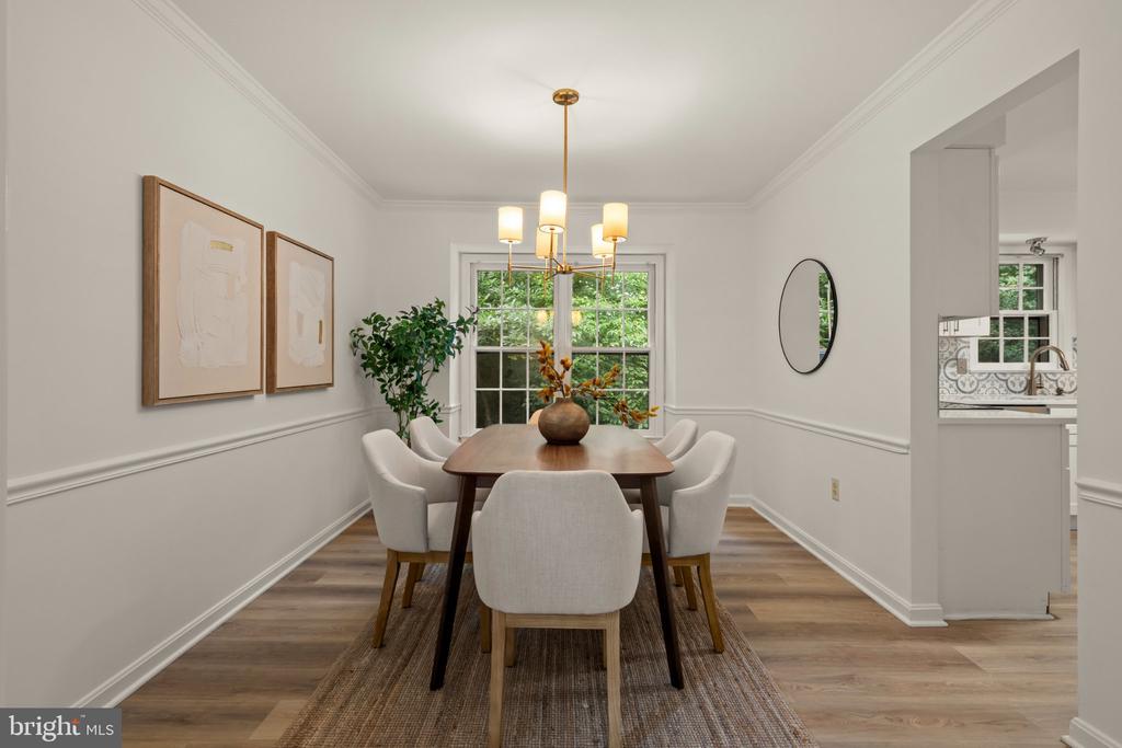 Staged dining room with a wood table, upholstered chairs, brass chandelier, and window overlooking greenery.