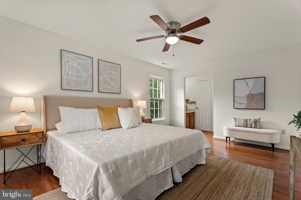 Bedroom with a white bed, mustard accent pillow, wood floors, and a ceiling fan.