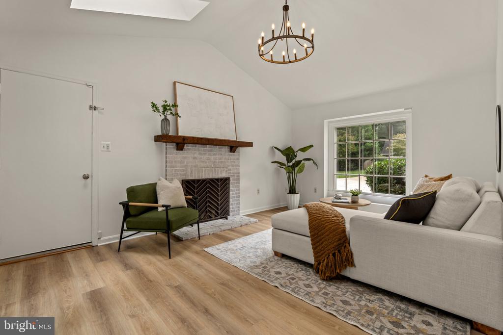 Living room with a brick fireplace, vaulted ceiling, and white sectional beside a large window.