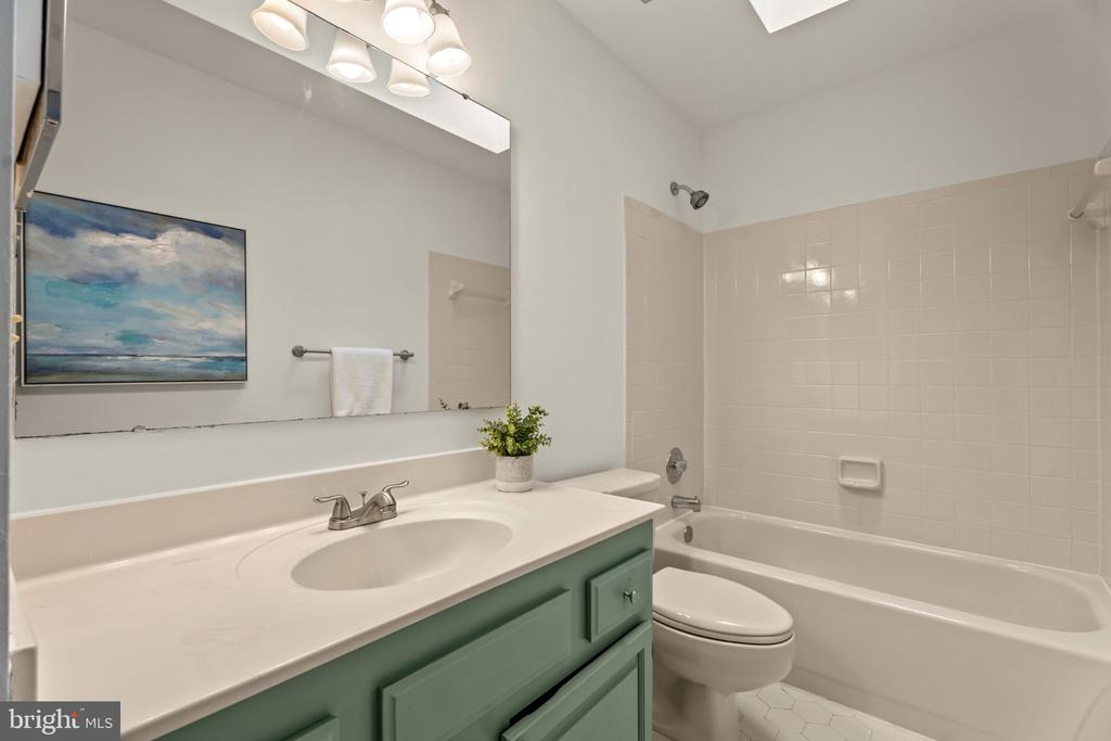 Bathroom with a green vanity, large mirror, and white bathtub with tiled surround.
