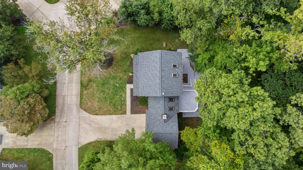 Aerial view of a gray-roofed house surrounded by mature trees, with its driveway visible.