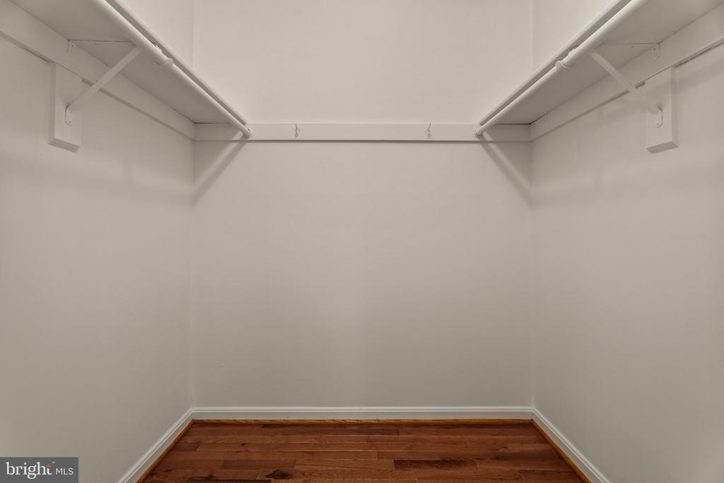 Empty walk-in closet with upper hanging rods and hardwood flooring.