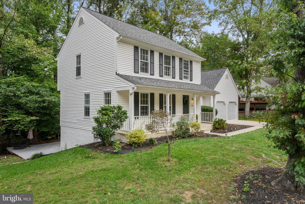 Two-story white house with a covered porch and attached garage, surrounded by mature trees.
