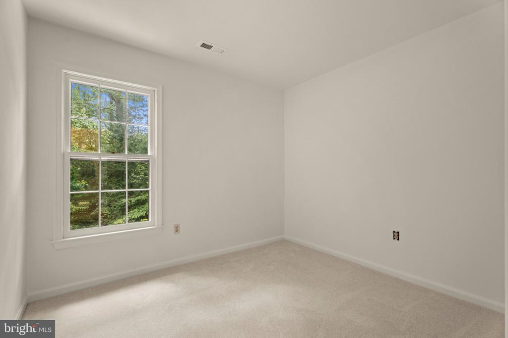 Empty carpeted room with a large divided window overlooking leafy trees.