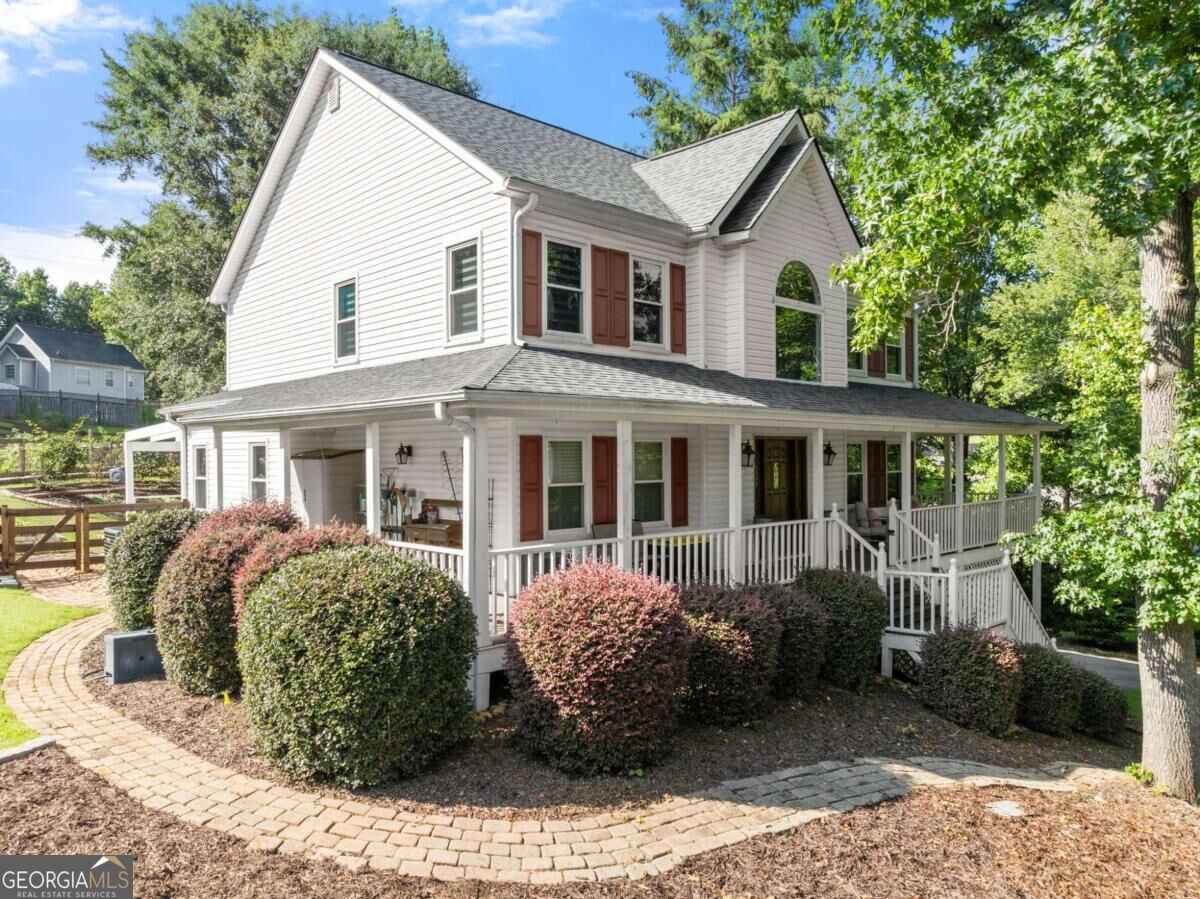 Two-story white house with red shutters, a wraparound porch, and curved brick walkways.